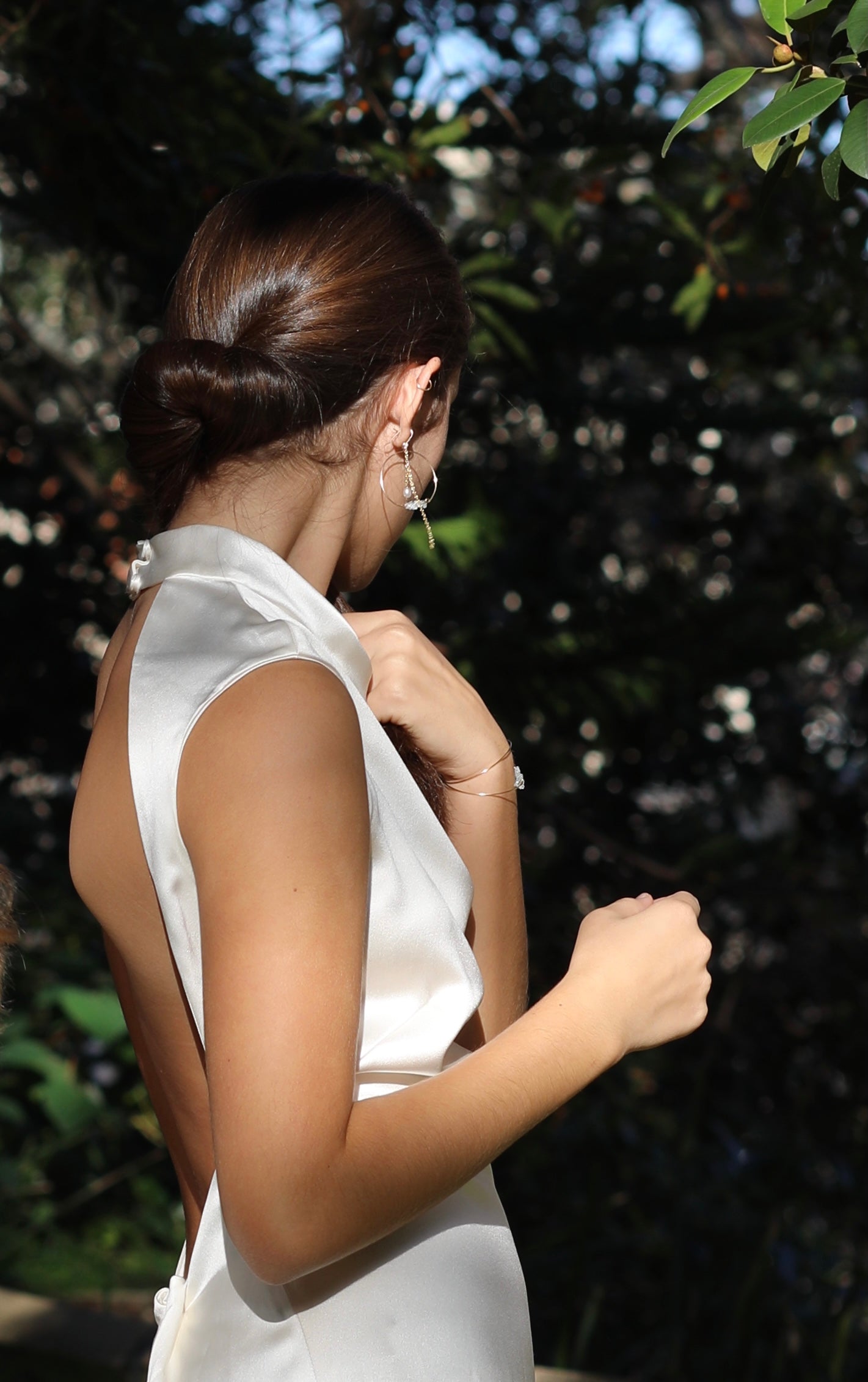Evelyn silk dress, high neckline backless dress white silk, top half of dress side view on model hair up greenery background