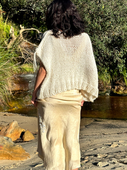 Sahara knitted wool vest, oversized cream sweater vest, sleeveless knitted vest in cream on model wearing eleanor silk dress back view standing up at beach waterfall