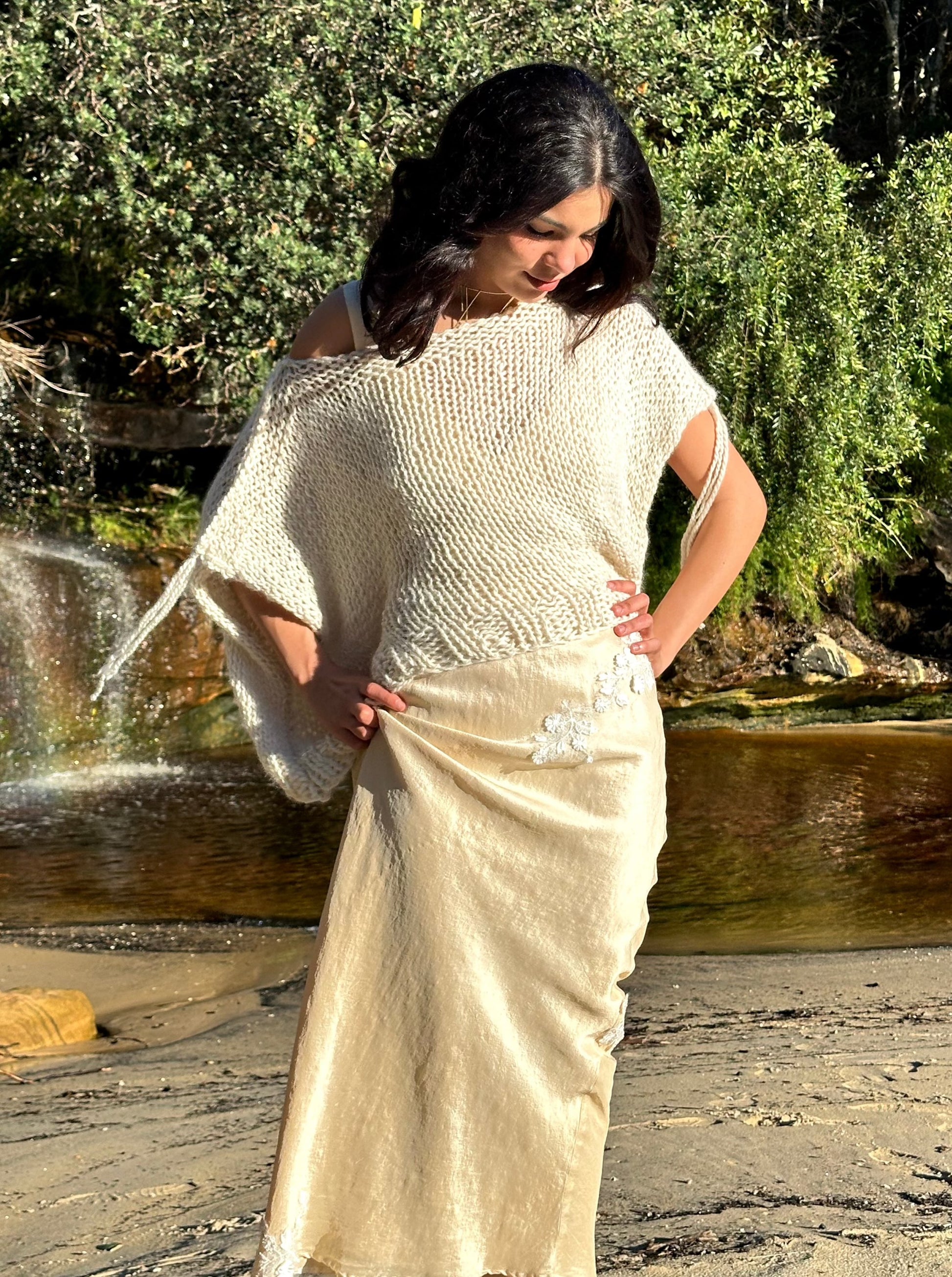 Sahara knitted wool vest, oversized cream sweater vest, sleeveless knitted vest in cream on model wearing eleanor silk dress standing up hands on hips at beach waterfall